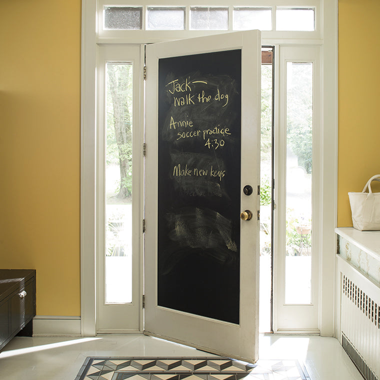 The back of a front door that has been painted black using Benjamin Moore's chalkboard paint, with a to do list written in yellow chalk.